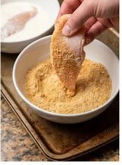 Chicken tender being coated in breadcrumbs