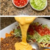 Nacho cheese being poured over Doritos and beef
